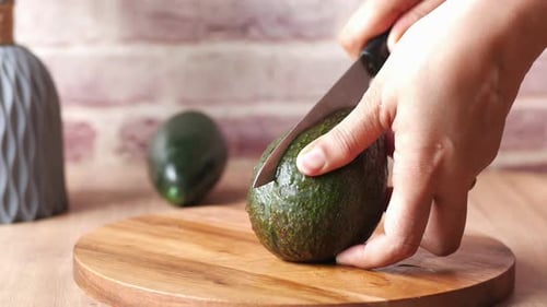 Hands Cutting Avocado on Wooden Cutting Board