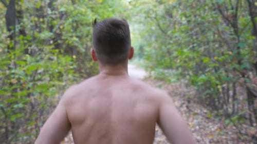 Young Muscular Man Running Along Trail at Early Autumn Forest