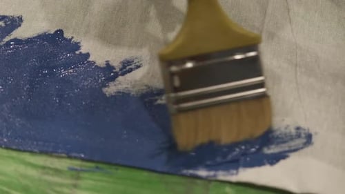 Paintbrush Applying Shiny Blue Paint to Fabric