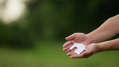 People cupped hands showing paper house
