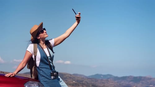 Entzückende positive, entspannte Touristin macht Selfie im Auto mit Smartphone