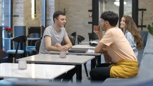 Side View of Positive Young Men Talking at the Table in Cafe As Woman Meeting Friend at the