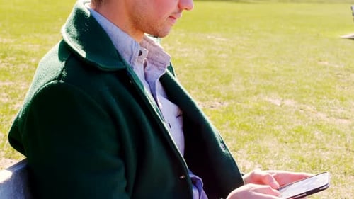 Man using mobile phone in the park on a sunny day 4k
