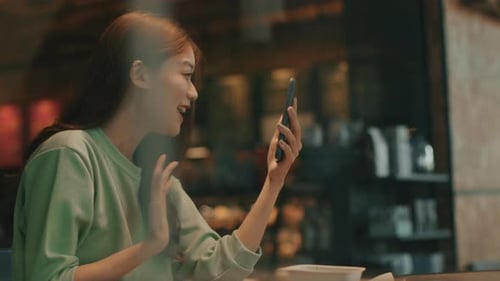 Asian woman using smartphone having video call with her friend, family sit in coffee shop