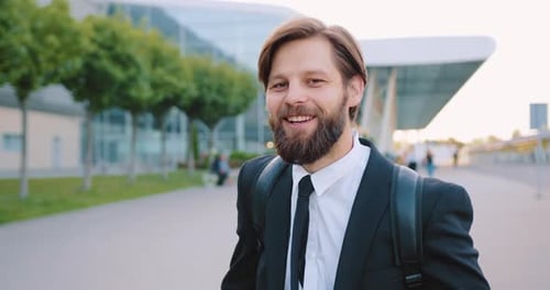 Hombre con barba bien cuidada con ropa elegante con mochila posando ante la cámara