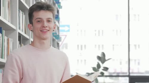 Cheerful Young Man Smiling While Reading a Book at College Library