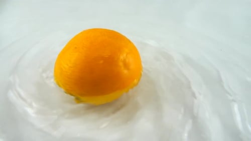 Rotating ripe orange in water on a white background. Slow motion.