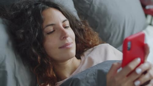 Woman Relaxing in Bed Looking at Smartphone