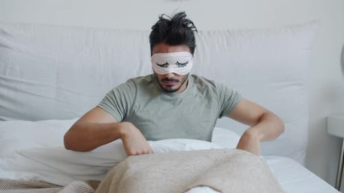 Portrait d'un homme arabe reposé se réveillant en enlevant son masque de sommeil et souriant au lit