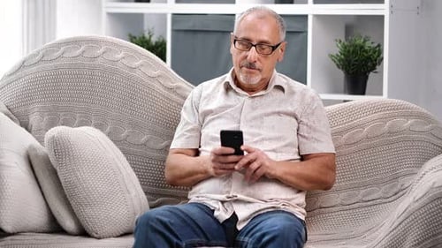 Gray-Haired Man Uses Phone on Couch at Home