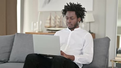 African Man with Laptop at Home Smiling at Camera