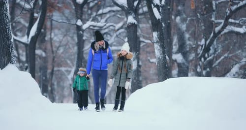 Young Woman Walks with a Girl and a Boy in a Park in Winter