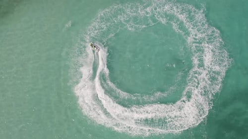 Aerial top view of jet ski or boat drawing a shape on sea ocean turquoise water. Adventure