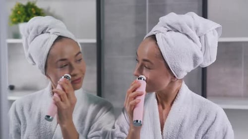Woman Using Beauty Roller for Facial Massage in Bathroom