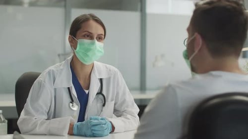 A Young Female Doctor in a Mask and Gloves is Receiving a Patient in a Medical Office