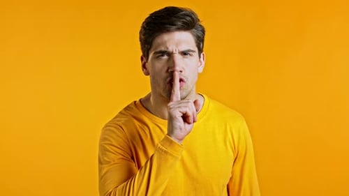 Handsome Man Holding Finger on His Lips Over Yellow Background. Gesture of Shhh, Hush, Secret