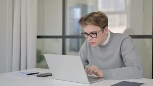 Young Man Celebrating Success While Using Laptop in Modern Office