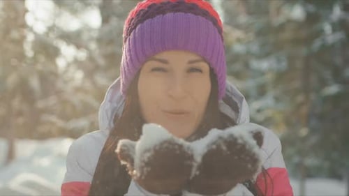 Young Woman Blowing Snow in Winter Forest