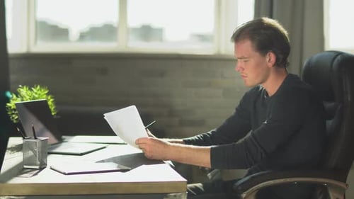 Young Thoughtful Businessman Sitting in the Office at the Table Near Notebook and Working