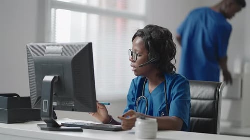 Médica general afroamericana negra con bata blanca sentada en el escritorio en el consultorio del médico