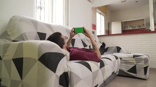 young man lying on the couch staring at his cell phone, green screen