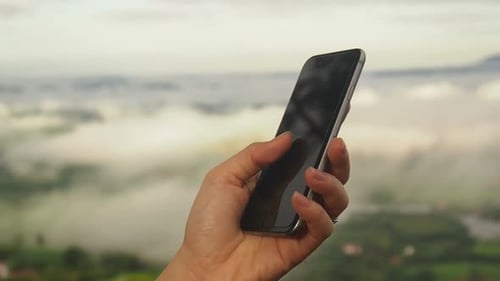 Hand Using Cellphone with Misty Mountain Background