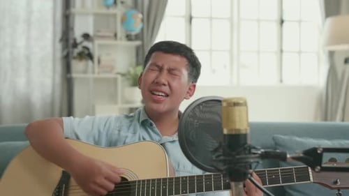Niño asiático tocando la guitarra y cantando una canción en casa