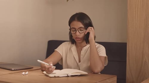 Woman Talking on Phone and Taking Notes at Desk