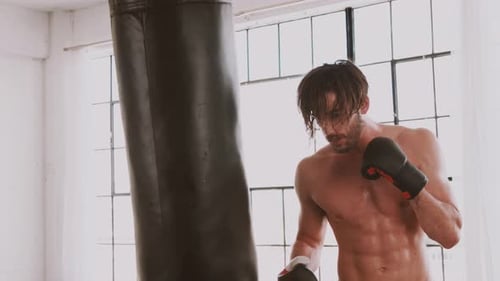 Shirtless Man Training Next to Boxing Bag in Gym