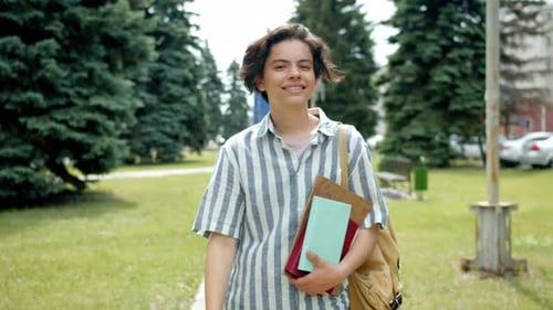 Cheerful Guy Walking Outdoors in Park Waving Hand Greeting Friends Holding Books