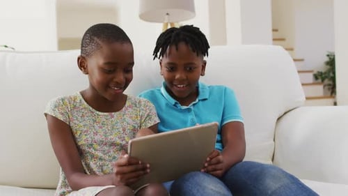 African american boy and girl using digital tablet while sitting on the couch at home