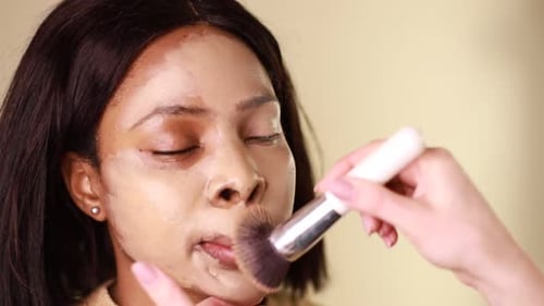 A female makeup artist applying gold makeup to a black African-American model.
