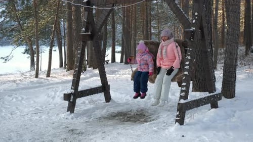 Girl and Woman Swinging Together on Snowy Day