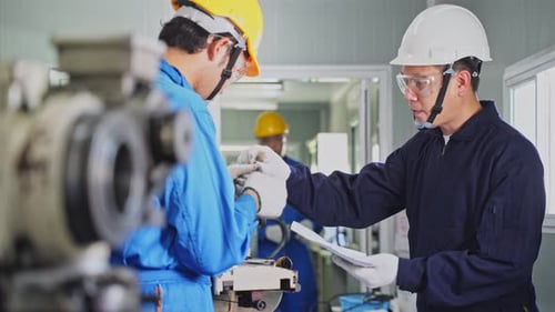 Asian mechanical workers technicians wearing helmet and working on milling machine in factory.