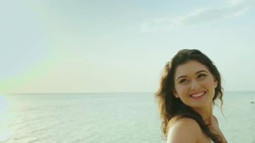 Young Woman Leads Behind Herself, Portrait. Goes Along the Beach, Smiles, Hair Croaks in the Wind