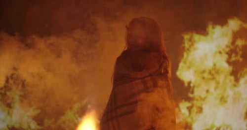 Child Standing near a Roaring Fire at Night