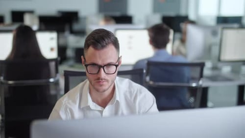 Serious Young Man Working on Decktop Computer While Working in Big Open Space Office