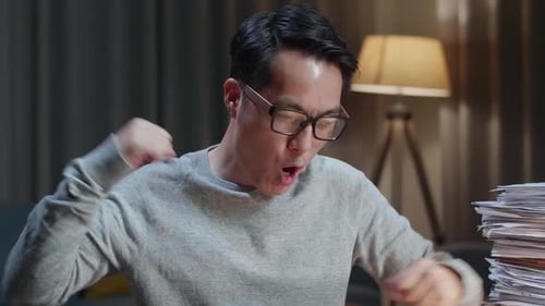 Cerca de feliz hombre asiático celebrando terminar de trabajar con documentos en casa