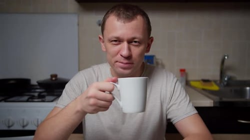 Porträt eines Mannes mit einer Tasse Tee am Tisch am Abend in der Küche, Kamerabewegung