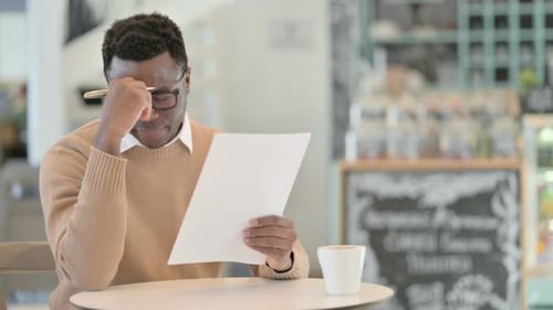 African American Man Reacting to Loss While Reading Documents in Cafe