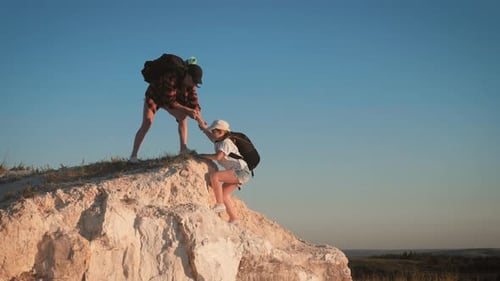 Girl Helps Her Friend Climb Up the Last Section of Mountain. Tourists with Backpacks Help Each Other