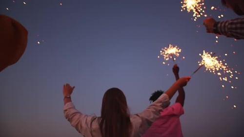 International friends in the evening in nature held lighted sparklers their hands background the sky