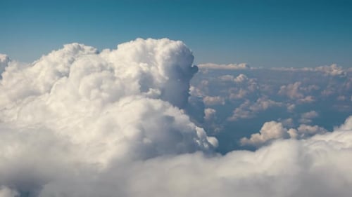 Aerial view from airplane window of white puffy clouds on bright sunny day.