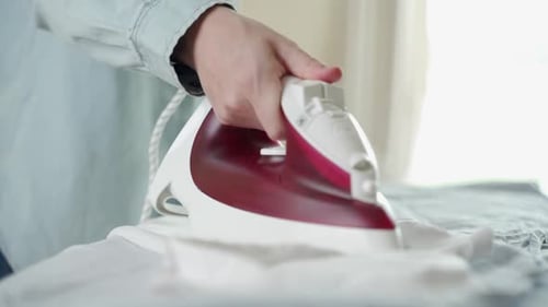 Hand of Woman Ironing Clothes on the Table