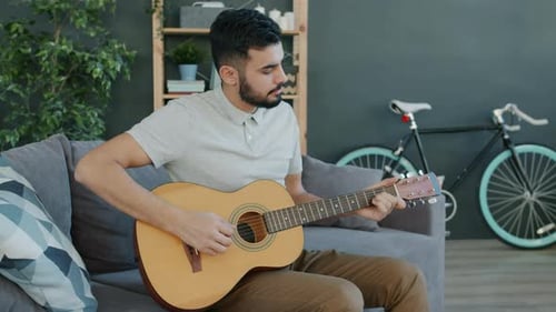 Young Man Plays Guitar on Couch at Home