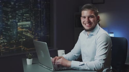 Smiling Young Adult Typing on Laptop at Night