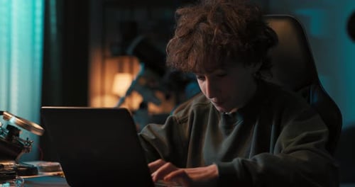 Young Adult Works on Laptop Computer at Desk Indoors