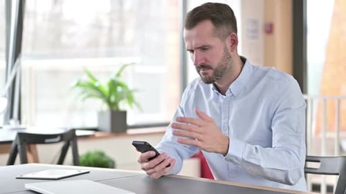 Young Man Reacting to Loss on Smartphone in Office