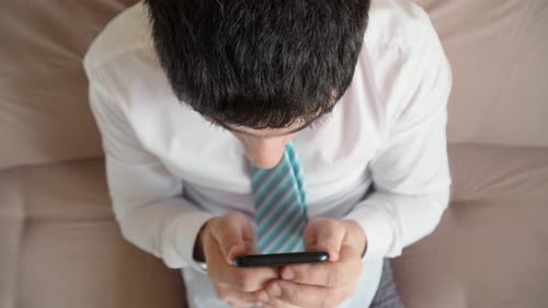 Man Excitedly Looks at Phone on Couch
