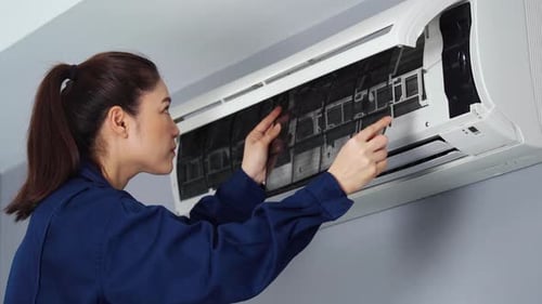 female technician service placing back clean filter into air conditioner